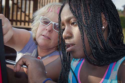 African american girl being shown by a mentor how to use assistive technology.