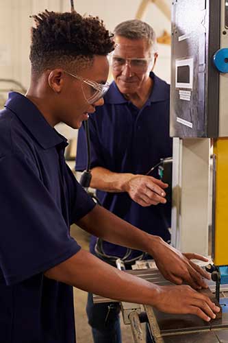 Young African American teen learning how to be a carpenter with his supervisor showing him how to use a piece of equipment.