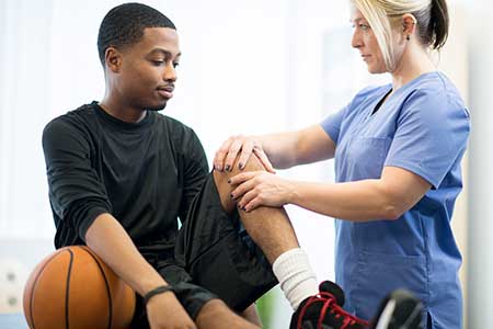 African American teen boy with a basketball having his knee being examined by a doctor.