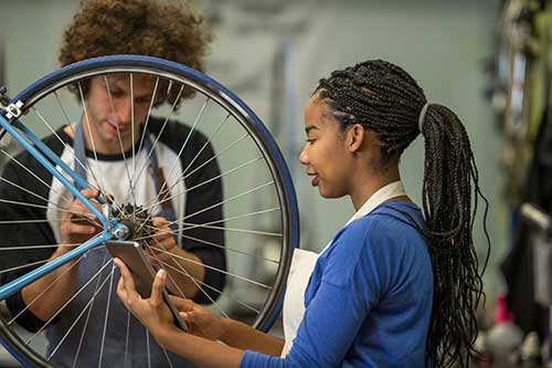 Two teens working on a bicycle in a repair store.